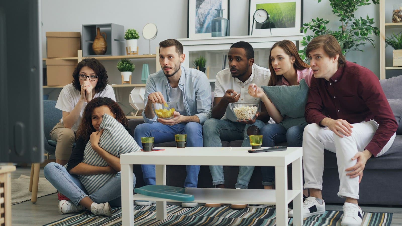 Un groupe d'amis assis sur un canapé suit avec attention un programme à la télévision